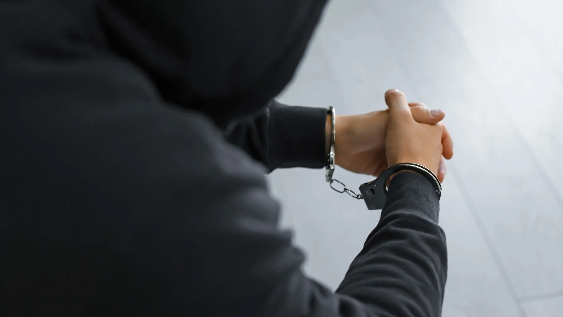 Eli kelepçeli kapşonlu bir adam oturuyor