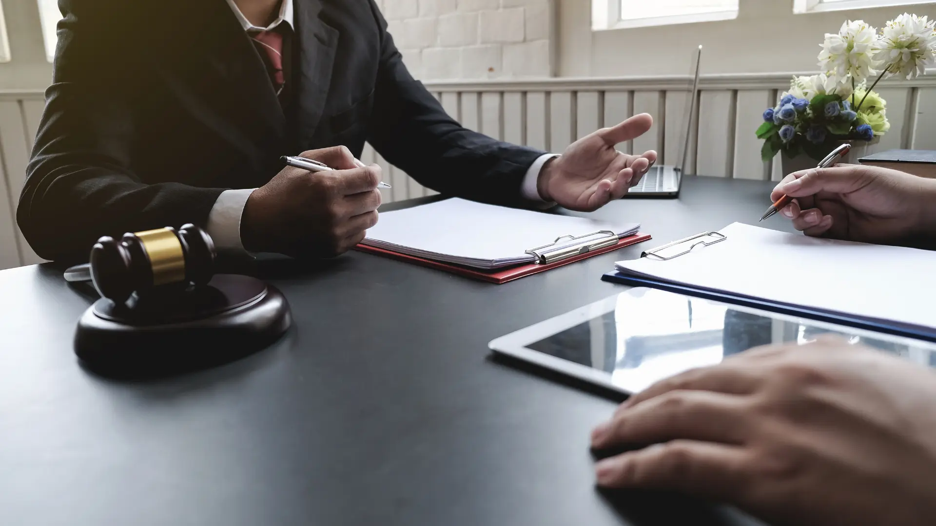 Takım elmiseli bir adam bir elinde kalem veönünde kağıtvar elinin yanında bir tokmak .Karşısında ise bir adam var .Adamın önünde bir tablet ve kağıt var ve elinde bir kalem var