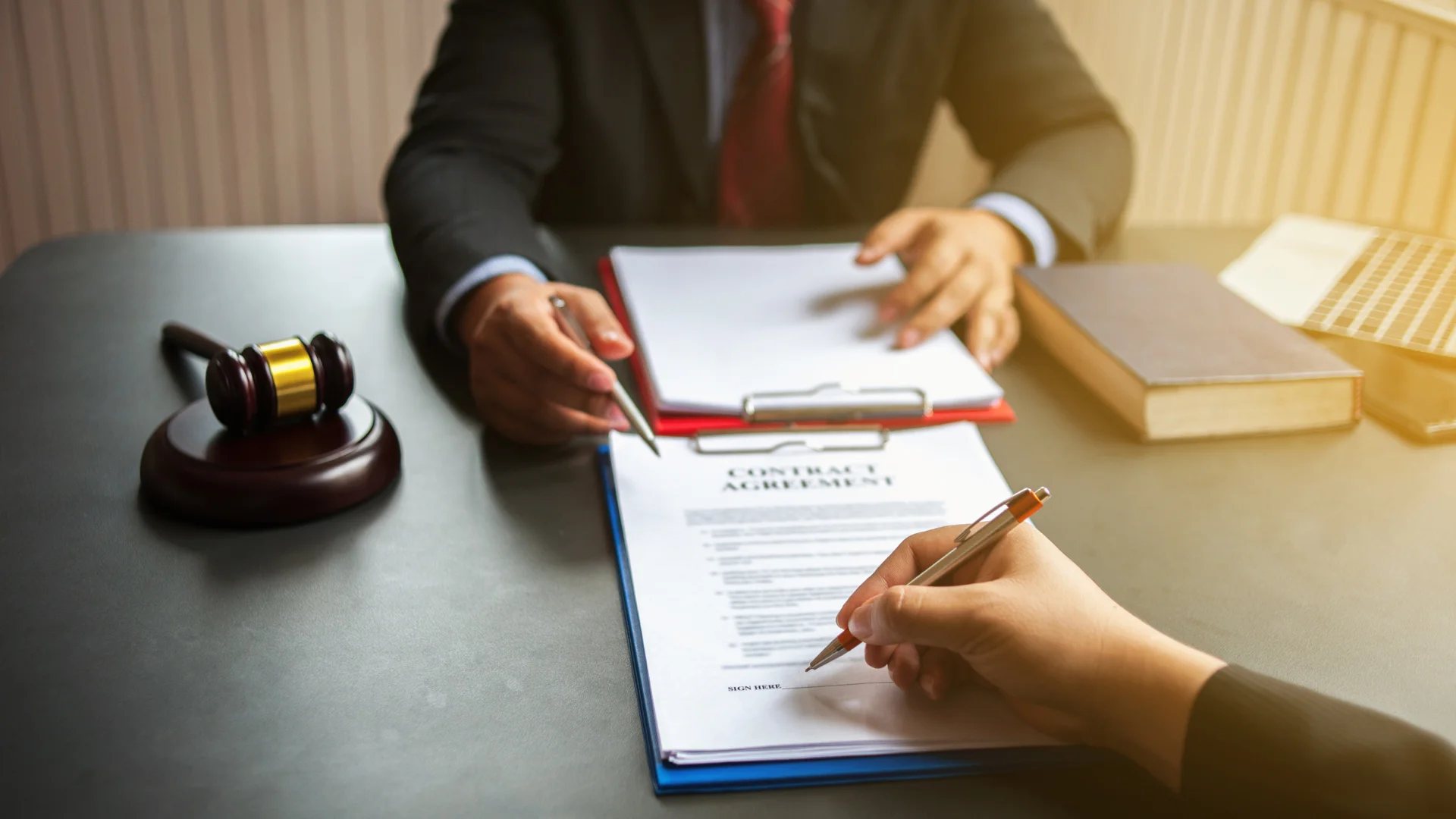 Bir avukat önünde iki sözleşme var ve bir sözleşmede elindeki kalmele bir yeri işaret ediyor ve karşısındaki kişi de orayı imzalıyor