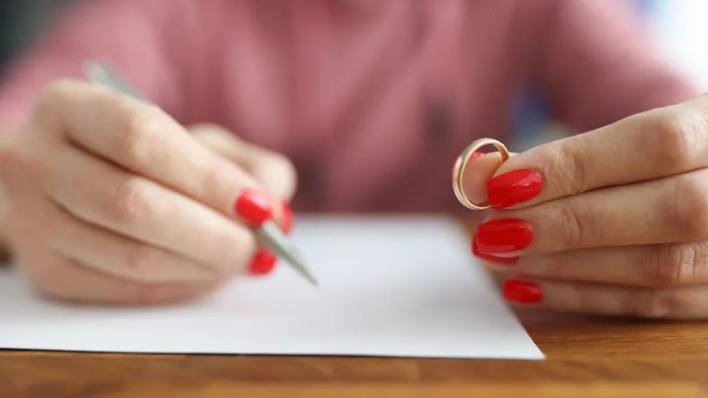 Kadının bir elinde yüzük diğer elinde kalem var ve kalem ile bir evrağı imzalıyor