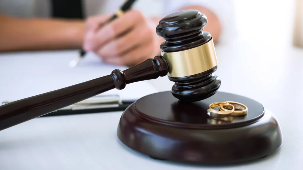 bir kişi elinde kalem ile bir kağıdı imzalıyor ve önünde bir tokmak üzerinde ise iki yüzük var