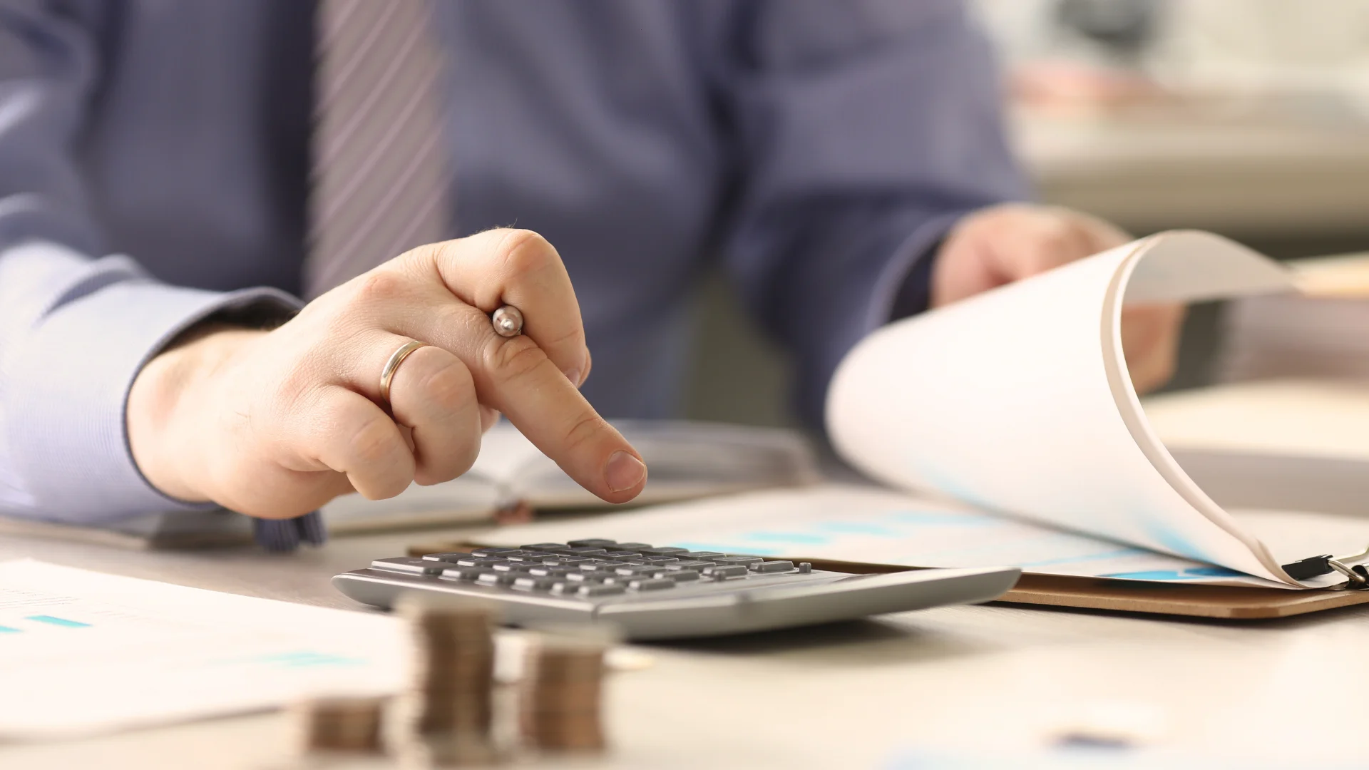 bir eliyle evrakalrı inceliyor diğer eliylede hesap makinesine veri girişi yapıyor.Hesap makinesiin yanında ise üst üste dizili bozuk paralr var