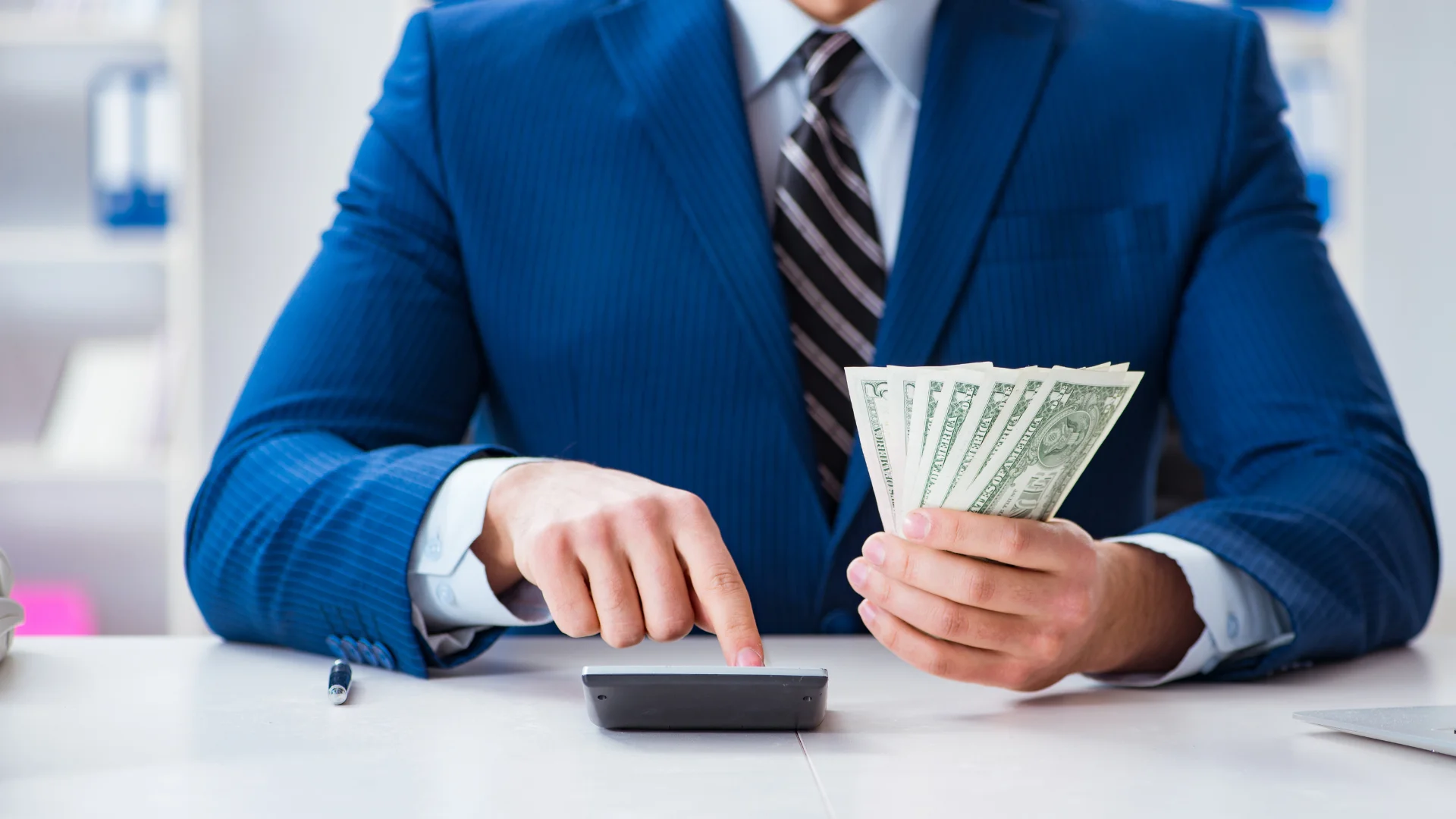 takim elbiseli kişi bir elinde para diğer eliyle hesap makinesinde hesaplama yapıyor